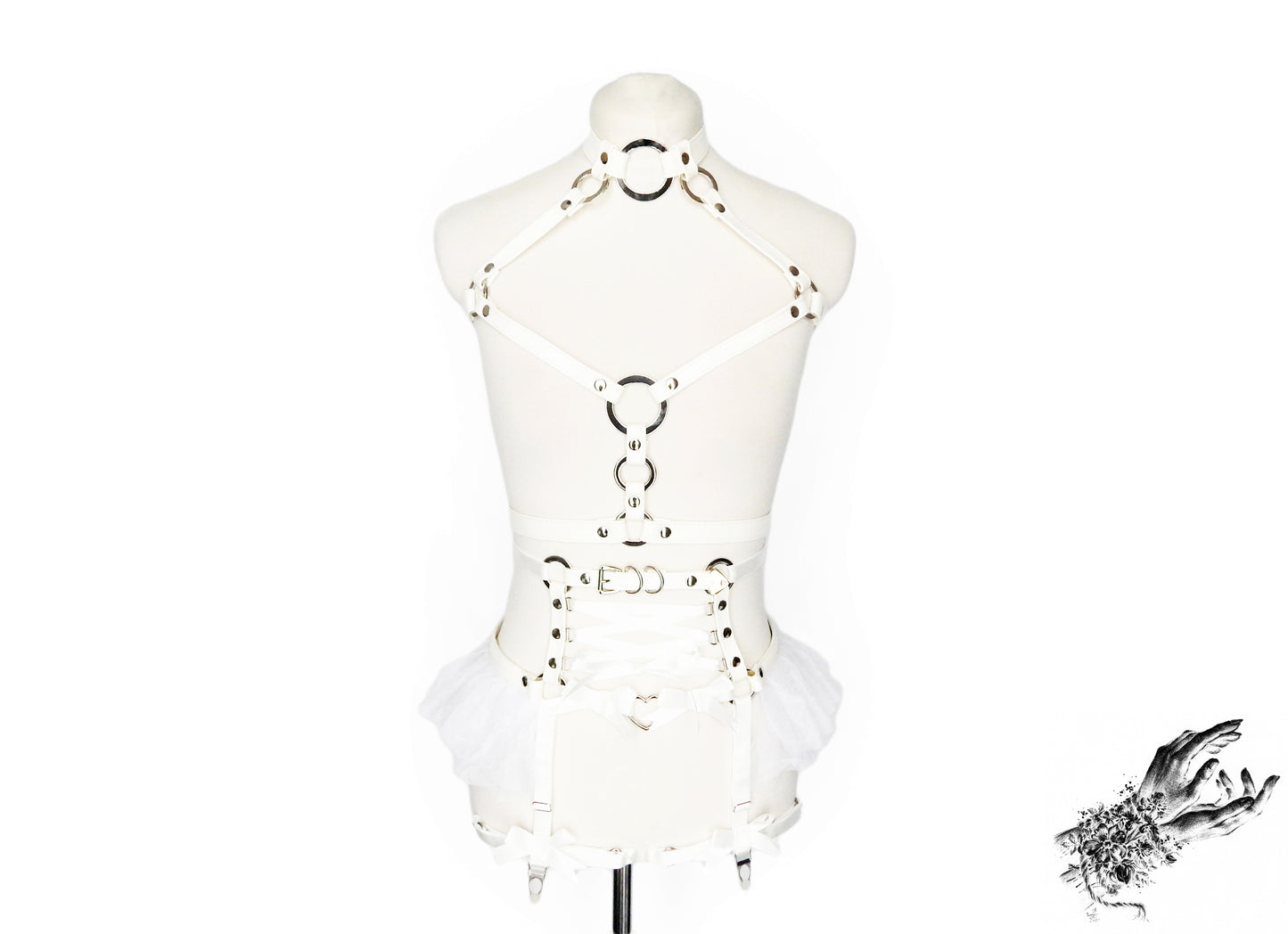 Front view of a white vegan leather harness set featuring a separate chest harness and garter belt with silver O ring hardware, white ruffled tulle accents and corset lacing at the waist, displayed on a mannequin against a white background.
