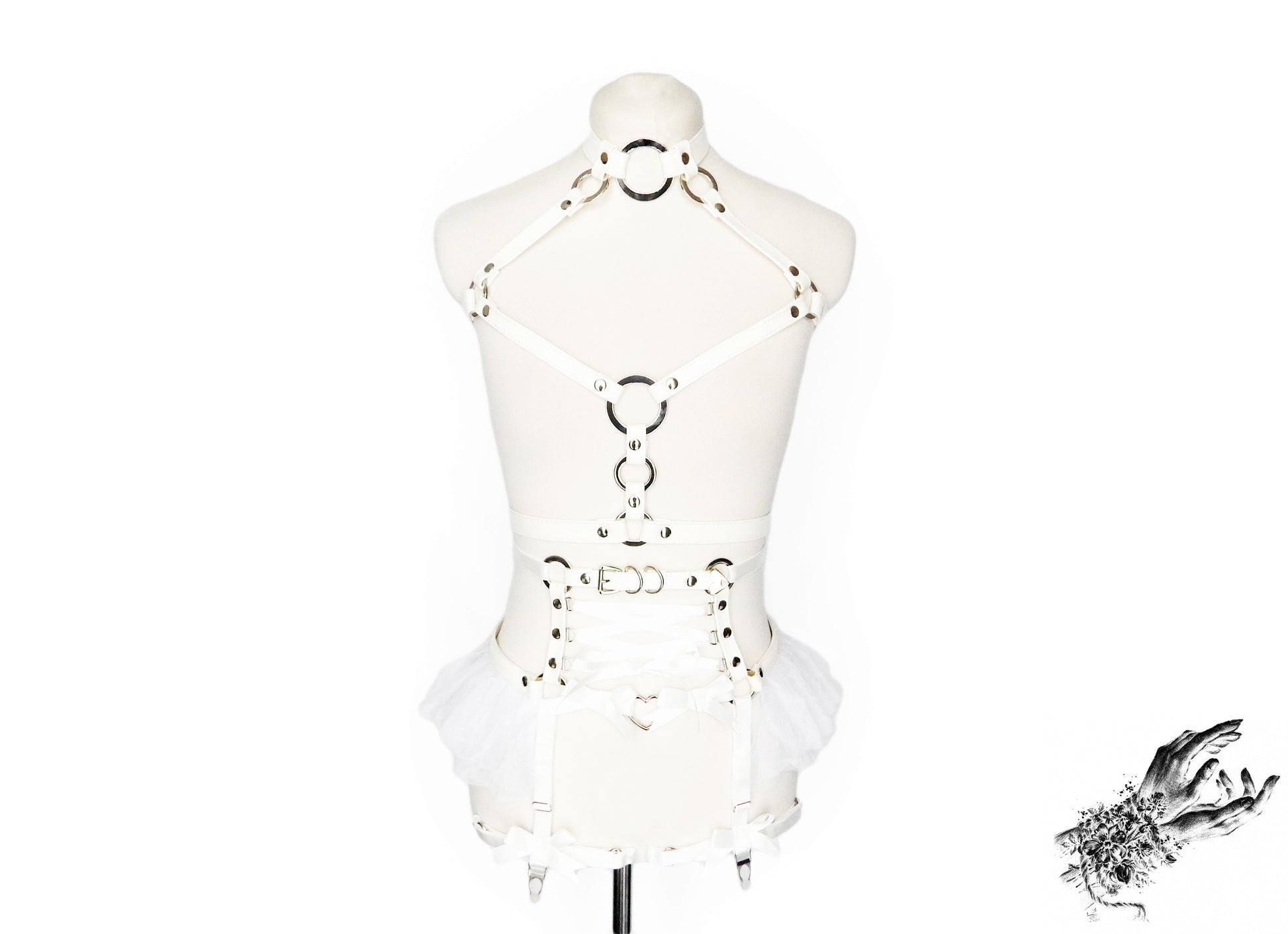 Front view of a white vegan leather harness set featuring a separate chest harness and garter belt with silver O ring hardware, white ruffled tulle accents and corset lacing at the waist, displayed on a mannequin against a white background.