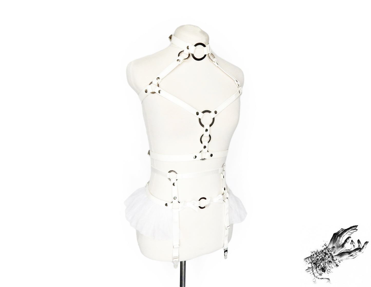 White faux leather harness set featuring a separate chest harness and garter belt with silver O ring hardware, white ruffled tulle accents at the waist and bow appliques, displayed on a mannequin against a white background.