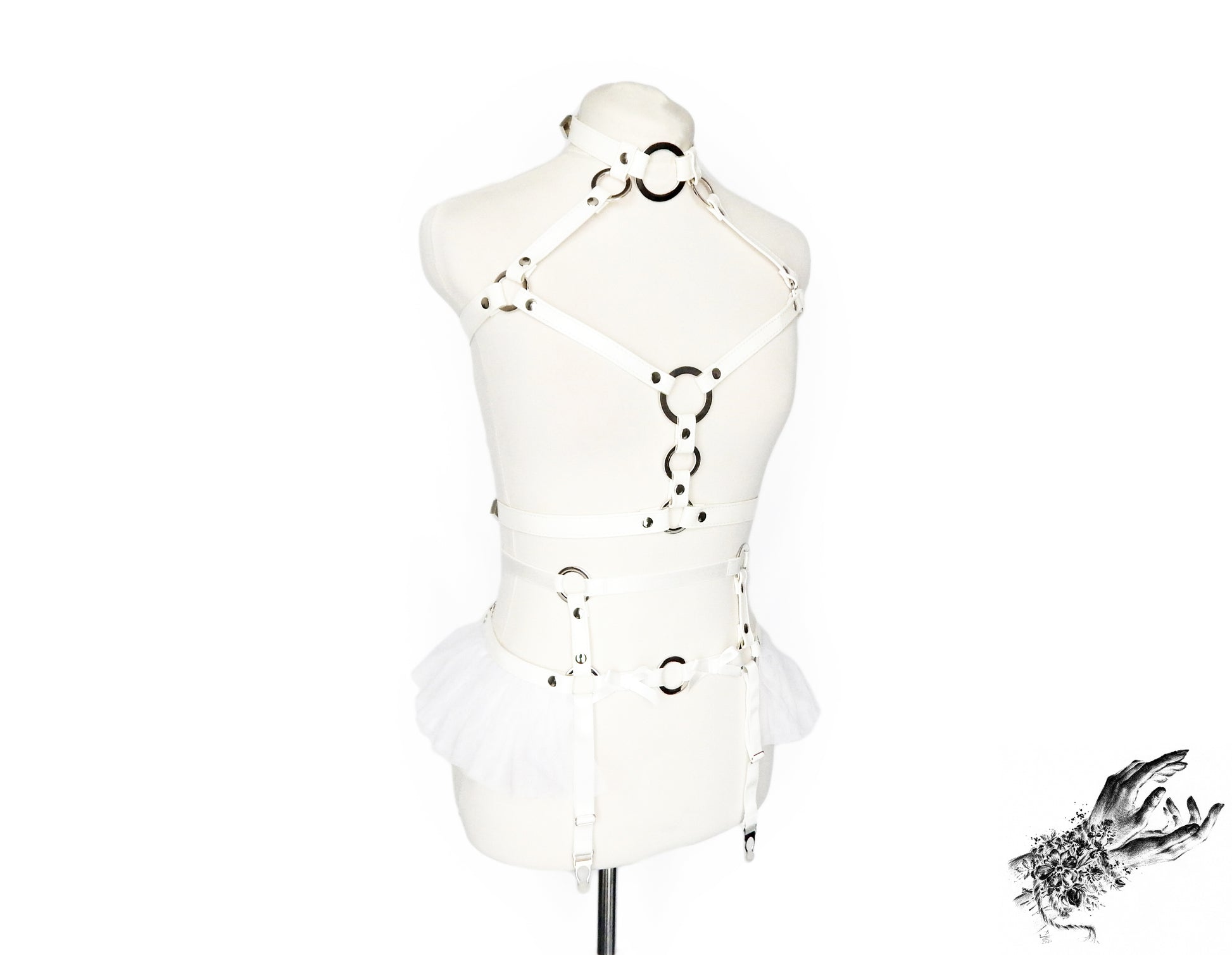 White faux leather harness set featuring a separate chest harness and garter belt with silver O ring hardware, white ruffled tulle accents at the waist and bow appliques, displayed on a mannequin against a white background.