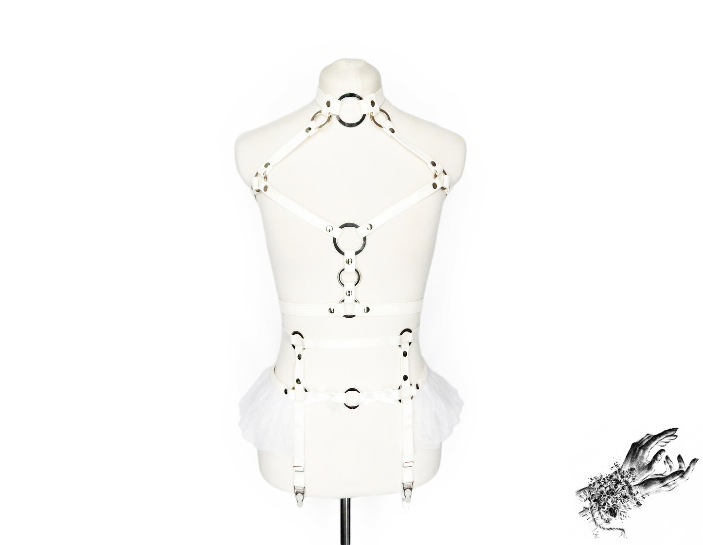 Front view of a white faux leather harness set featuring a separate chest harness and garter belt with silver O ring hardware, white ruffled tulle accents at the waist and bow appliques, displayed on a mannequin against a white background.