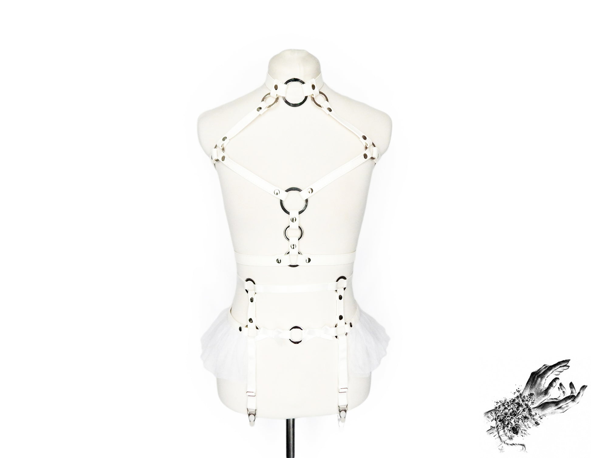 Front view of a white faux leather harness set featuring a separate chest harness and garter belt with silver O ring hardware, white ruffled tulle accents at the waist and bow appliques, displayed on a mannequin against a white background.