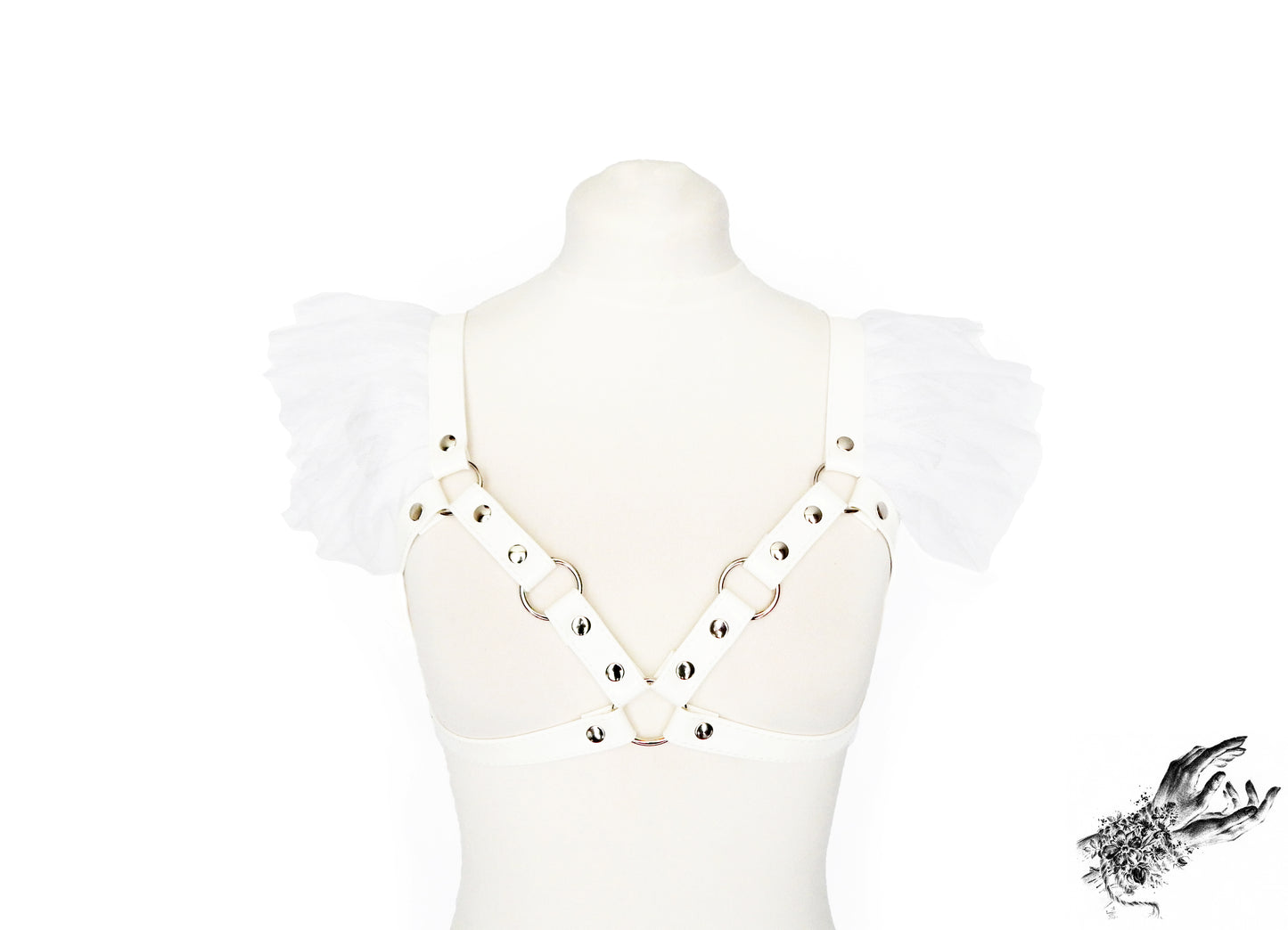 White faux leather harness bra featuring ruffled tulle accents at the shoulders, silver O ring hardware and adjustable body straps, displayed on a mannequin against a white background.