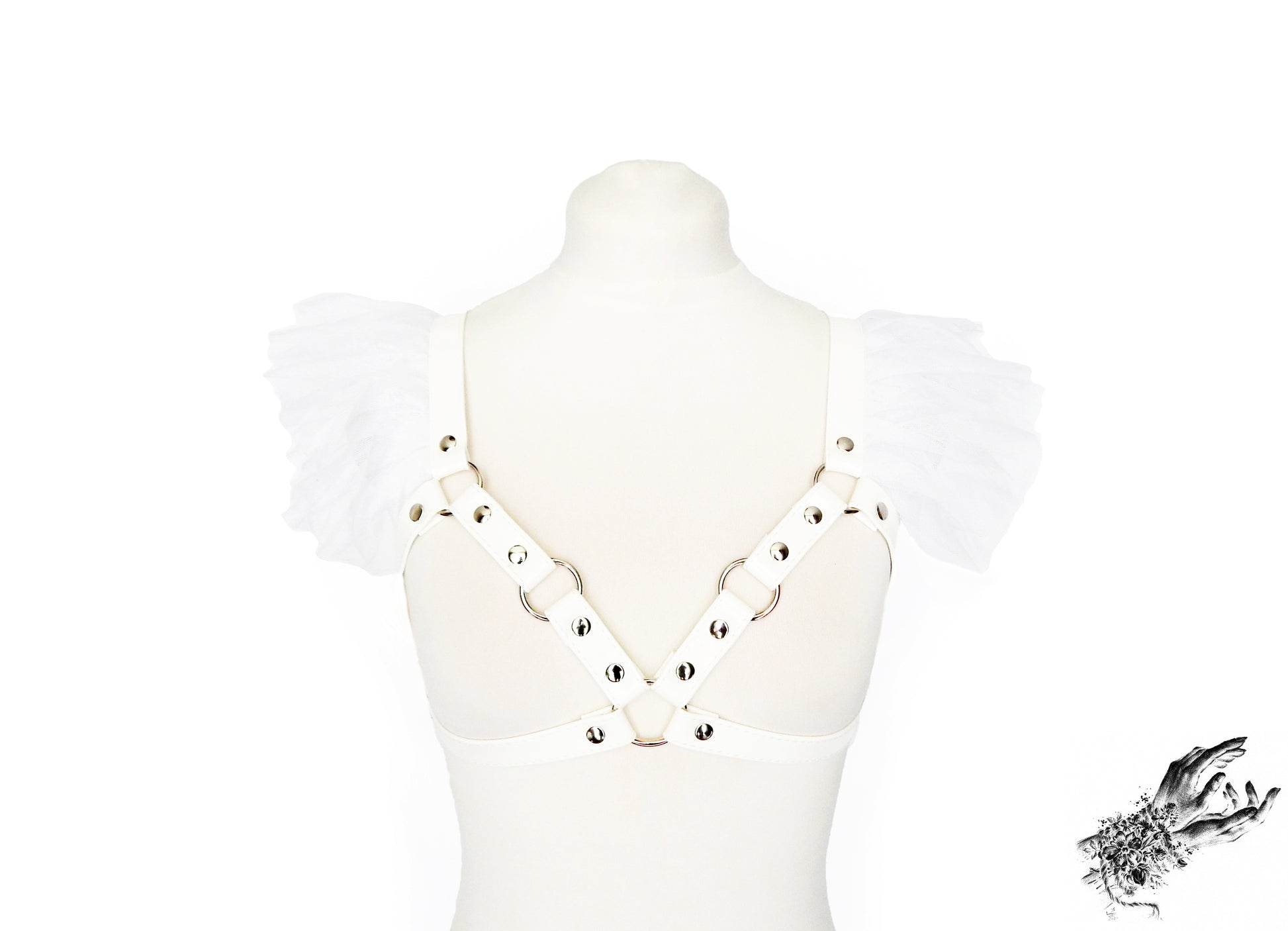 White faux leather harness bra featuring ruffled tulle accents at the shoulders, silver O ring hardware and adjustable body straps, displayed on a mannequin against a white background.