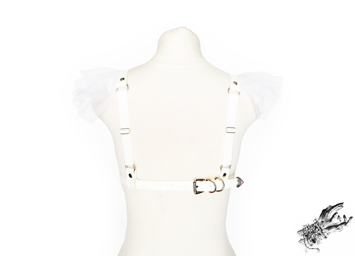 Rear view of a white faux leather harness bra featuring ruffled tulle accents at the shoulders, adjustable elastic shoulder straps and buckled vegan leather underbust strap, displayed on a mannequin against a white background.