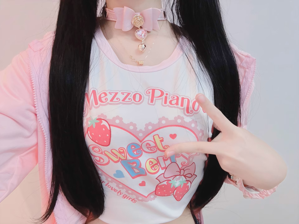 Worn photo of a pink leather choker featuring a central bow shaped design, gold tone rose and heart studs with detachable pink and gold crystal heart and bell charm. Styled with black pigtails and a pastel pink graphic t-shirt for a Fairy Kei fashion aesthetic.