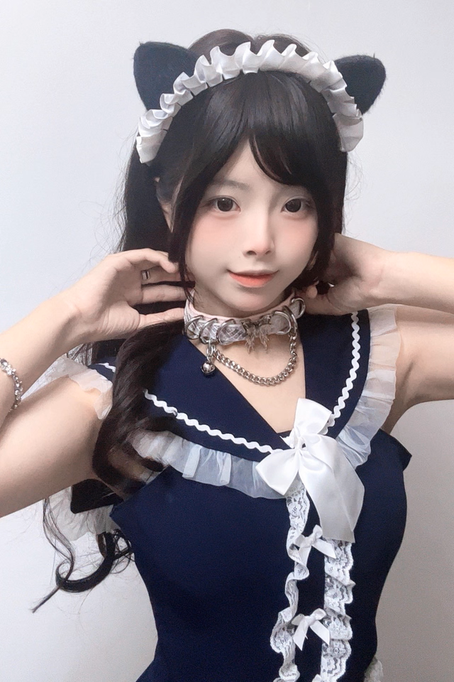 Worn photo of a pink and holographic silver leather choker featuring a stainless steel plated butterfly charm, D rings, chain and bell. Styled with black and white cat ears and maid costume for a kawaii idol aesthetic.