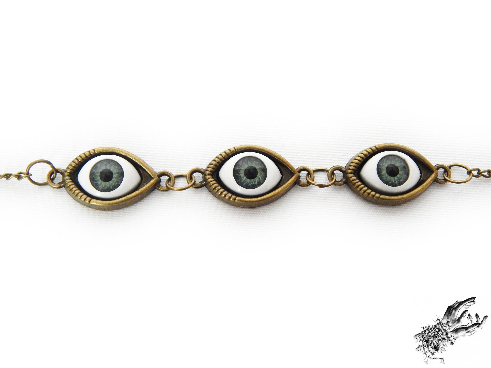 Close-up of the antique bronze evil eye bracelet showing striking green irises in bronze cameo frames for a vintage fashion aesthetic, displayed on a white background