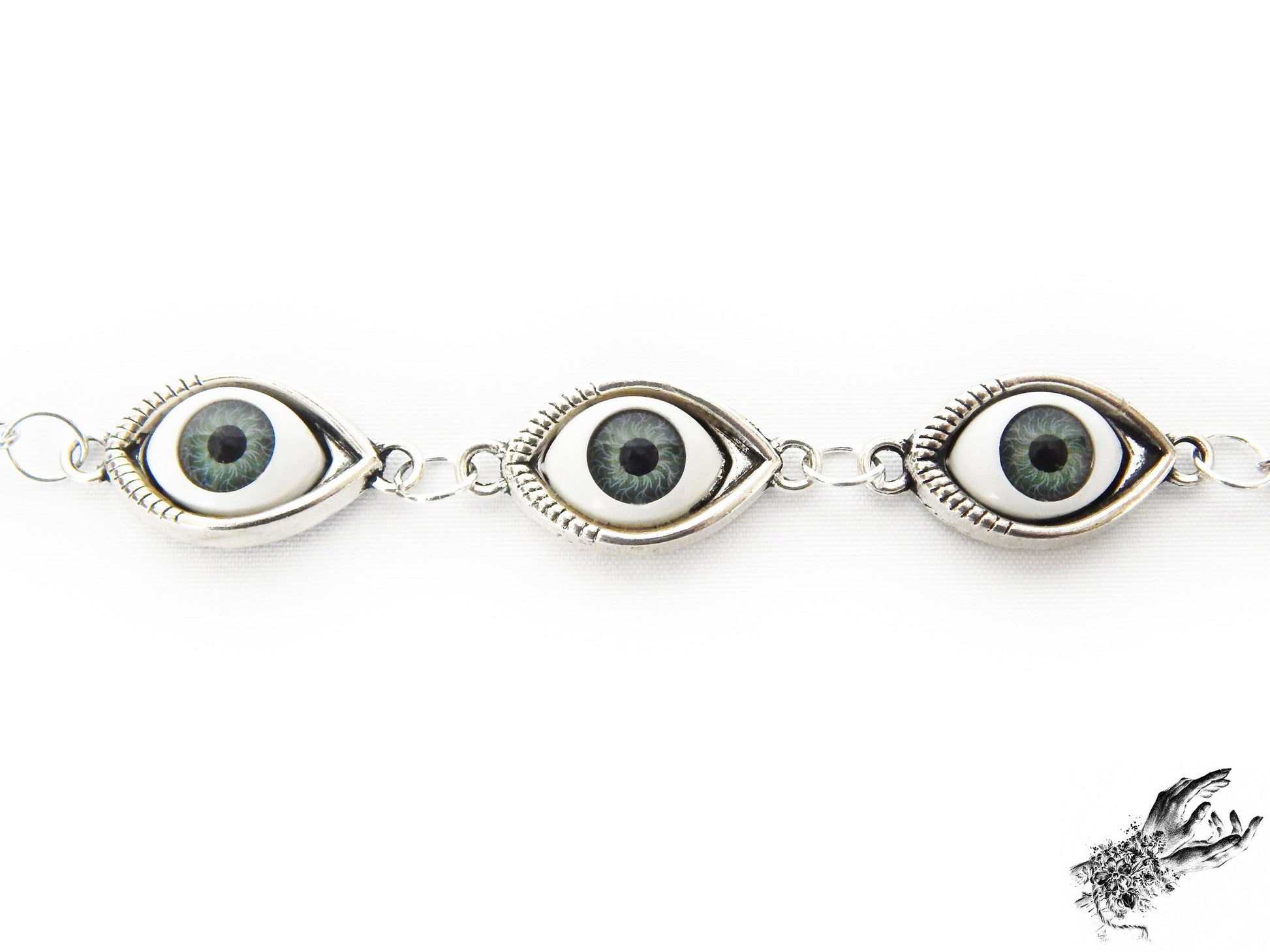 Close-up of the antique silver evil eye bracelet showing striking green irises in silver cameo frames for a vintage fashion aesthetic, displayed on a white background