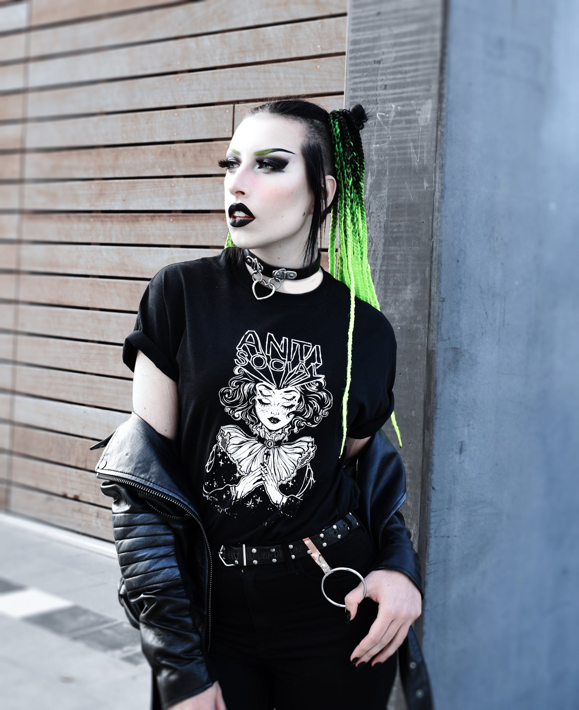 Black leather choker with a silver heart-shaped pendant styled with black and green braided hair, black graphic t-shirt and leather jacket for a nu goth look