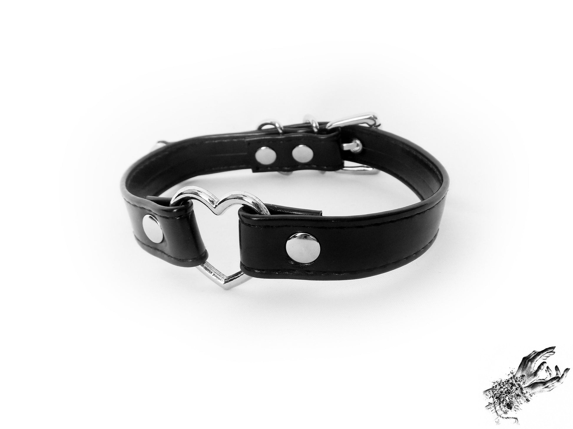 Black faux leather choker featuring a central silver tone heart ring, stainless steel plated hardware and adjustable buckle fastening at the back. Displayed on a white background.