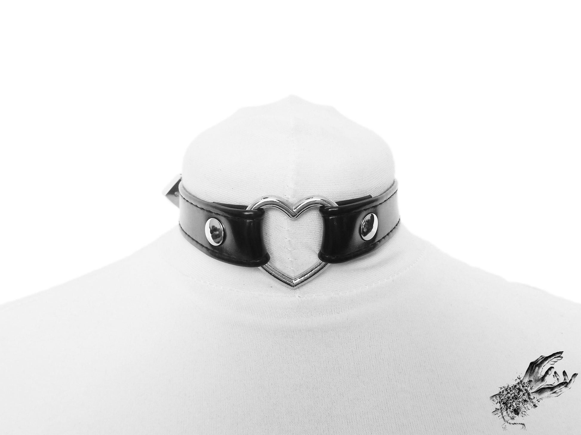 Black faux leather choker featuring a central silver tone heart ring, stainless steel plated hardware and adjustable buckle fastening at the back. Displayed on a white mannequin bust against a white background.
