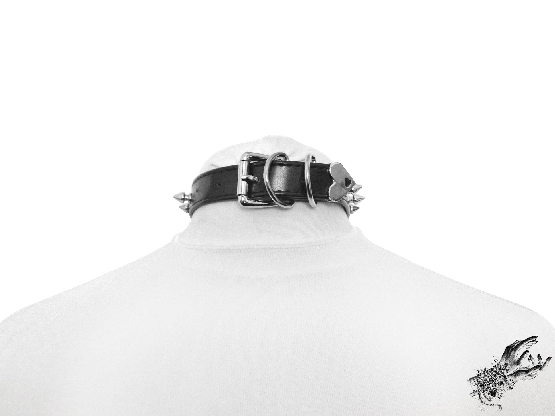 Rear view of a black faux leather choker featuring a central silver tone heart ring, stainless steel plated hardware and adjustable buckle fastening at the back. Displayed on a white mannequin bust against a white background.