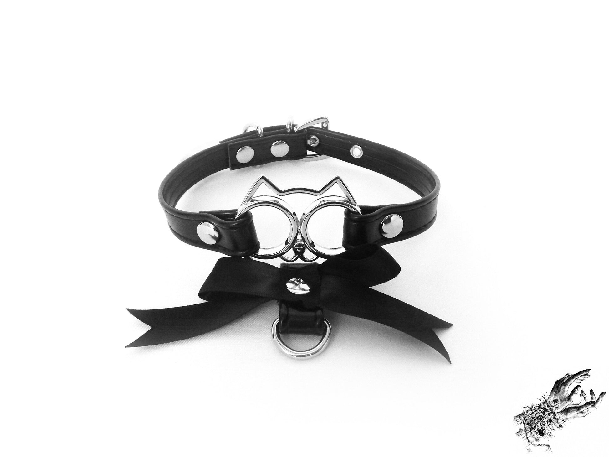 Black faux leather choker featuring a central silver cat shaped pendant and black satin ribbon charm, for a kawaii gothic aesthetic, displayed on a white background