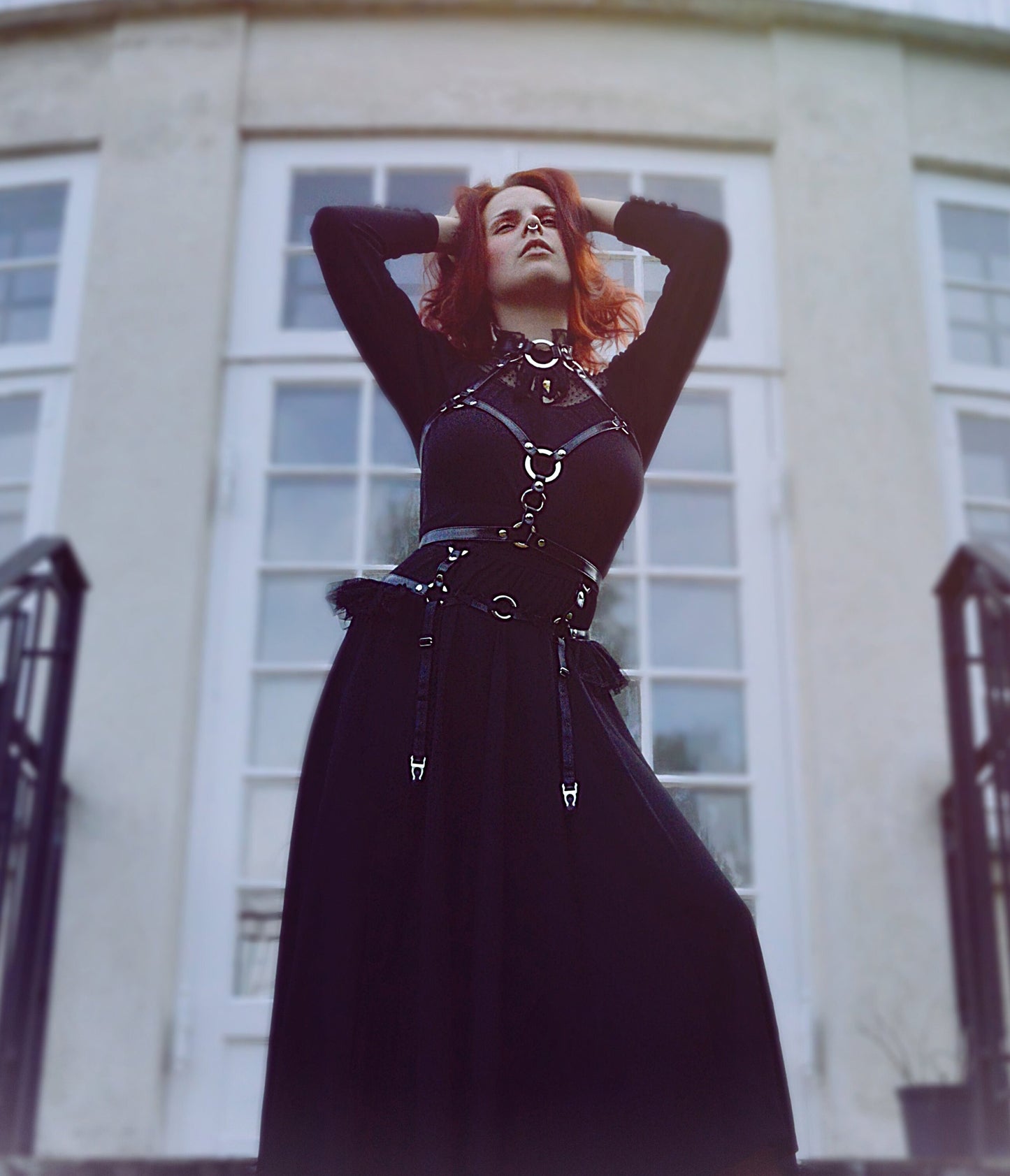 Modelled photo of a black vegan leather O ring harness set, styled with a long black Victoriana style dress and bright red hair in a stately home setting for a Penny Dreadful inspired look.