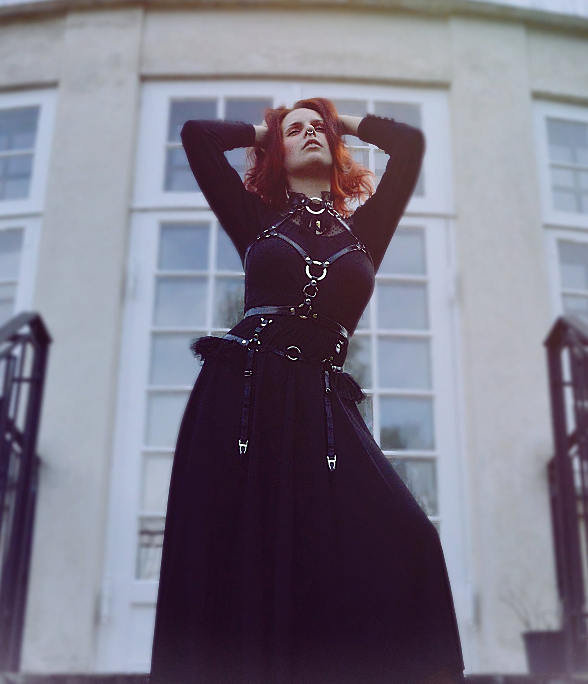 Modelled photo of a black vegan leather O ring harness set, styled with a long black Victoriana style dress and bright red hair in a stately home setting for a Penny Dreadful inspired look.