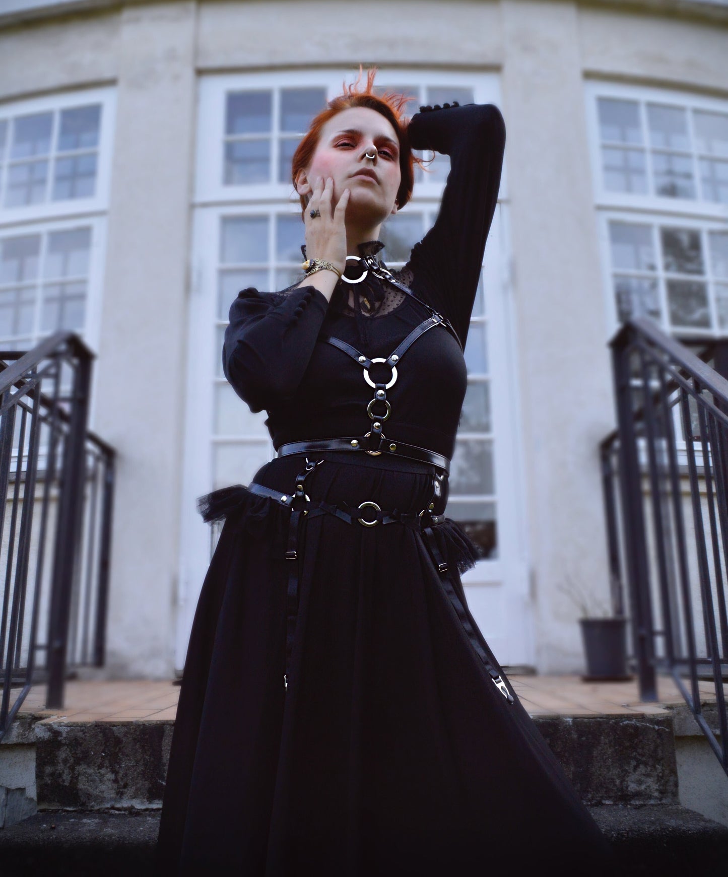 Modelled photo of a black vegan leather O ring harness set, styled with a long black Victoriana style dress, bright red hair and romantic make-up in a stately home setting for a Penny Dreadful inspired look.