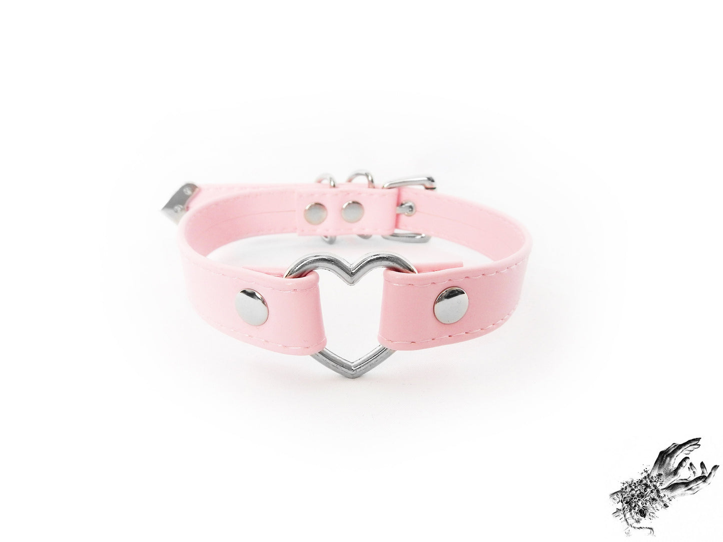 Pink faux leather choker featuring a central silver tone heart ring, stainless steel plated hardware and adjustable buckle fastening at the back. Displayed against a white background.