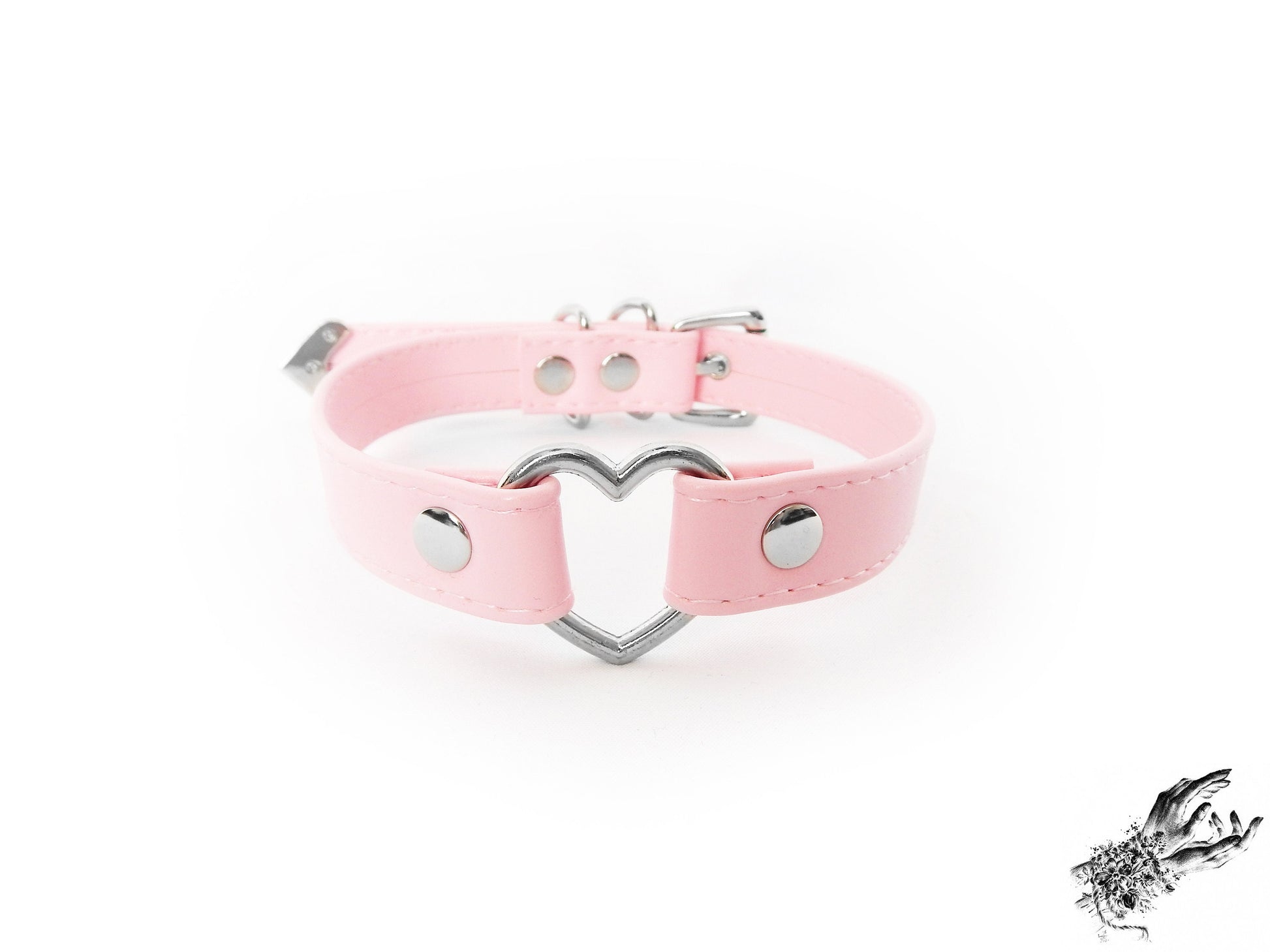 Pink faux leather choker featuring a central silver tone heart ring, stainless steel plated hardware and adjustable buckle fastening at the back. Displayed against a white background.