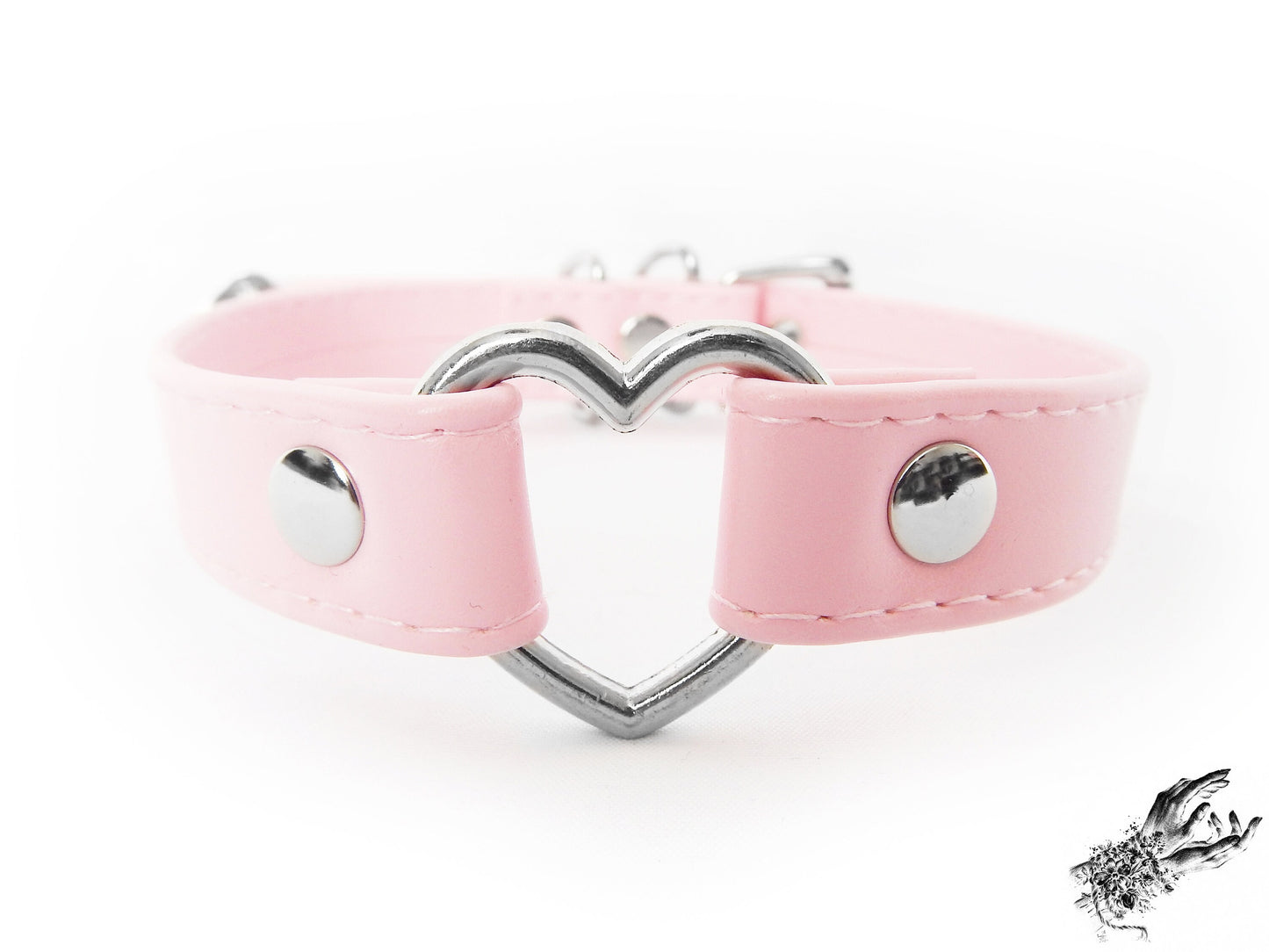 Close-up of a pink faux leather choker featuring a central silver tone heart ring, stainless steel plated hardware and adjustable buckle fastening at the back. Displayed against a white background.