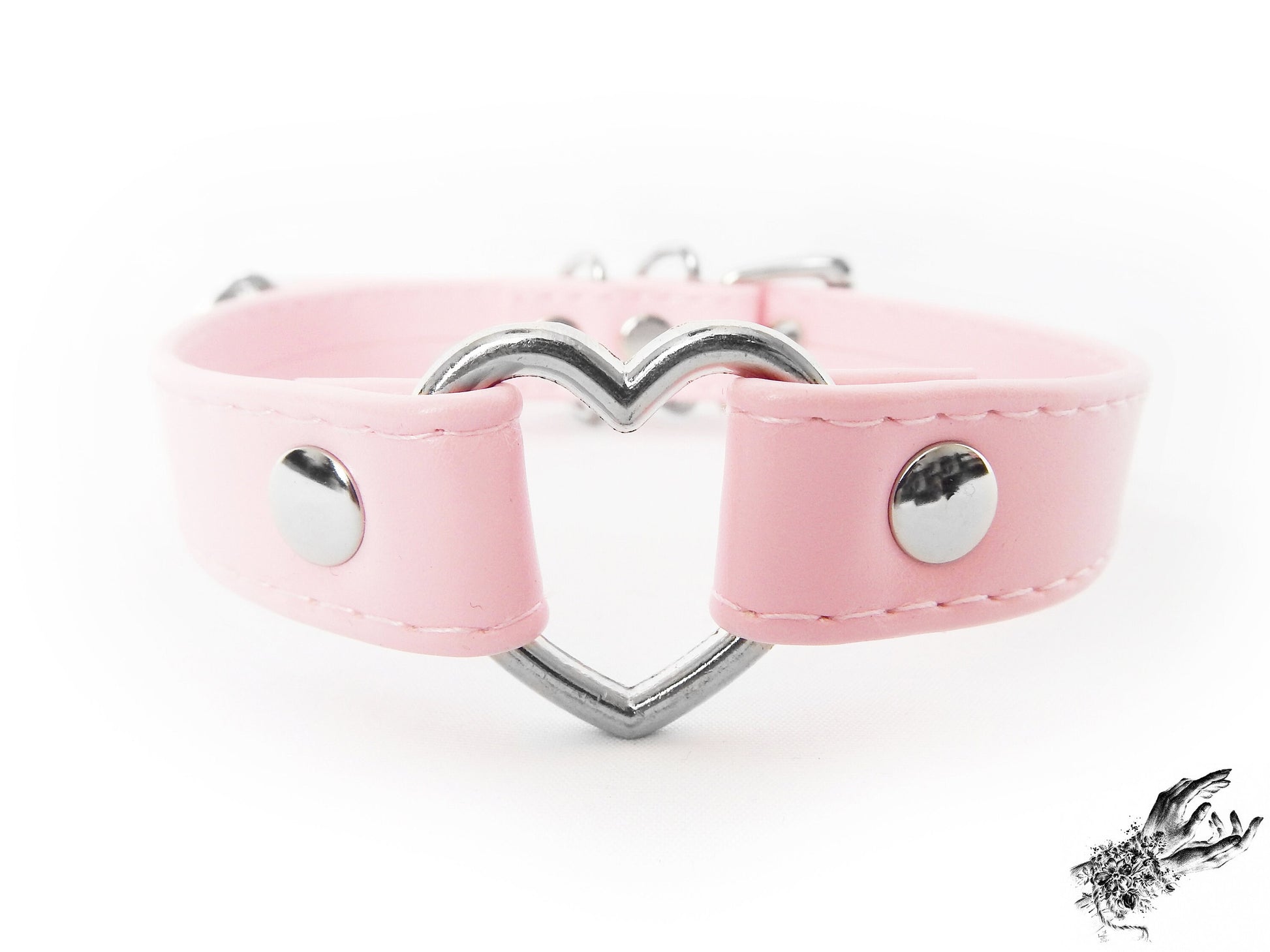 Close-up of a pink faux leather choker featuring a central silver tone heart ring, stainless steel plated hardware and adjustable buckle fastening at the back. Displayed against a white background.