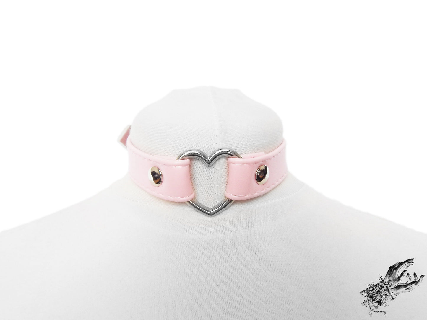 Pink faux leather choker featuring a central silver tone heart ring, stainless steel plated hardware and adjustable buckle fastening at the back. Displayed on a white mannequin bust against a white background.