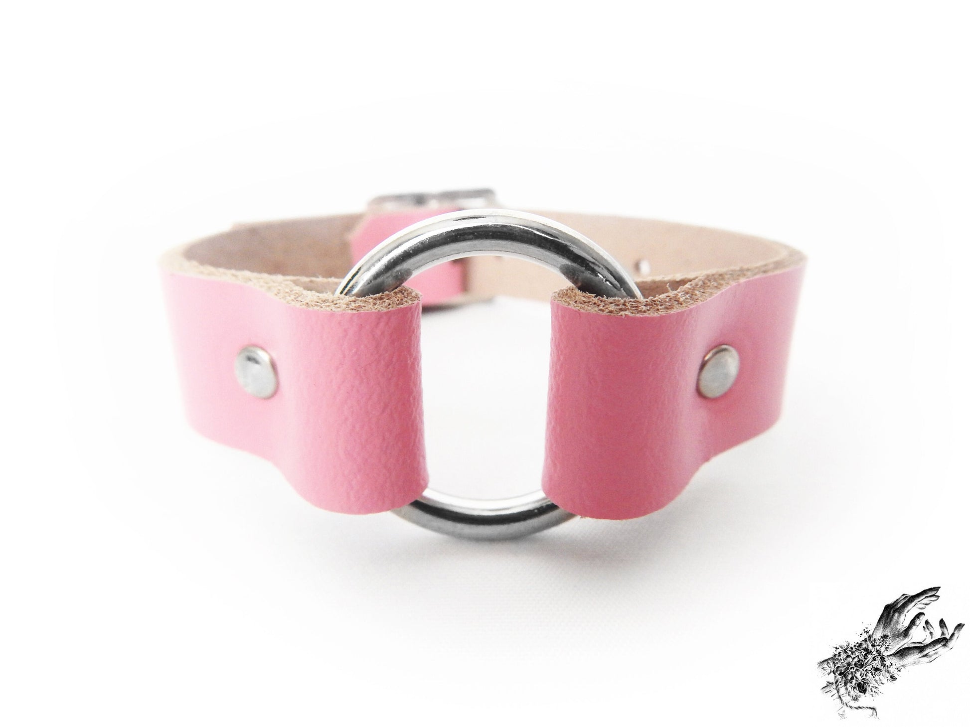 Close-up of the pink leather wristband featuring a central silver O ring and durable silver rivets on a white background