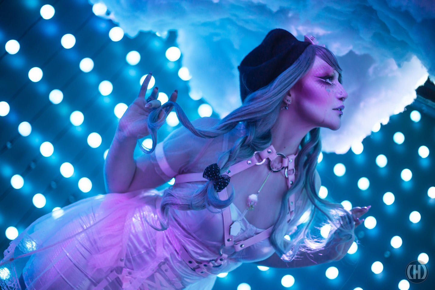 Modelled photo of a pink vegan leather O ring and corset harness set, styled with a sheer pink organza dress and striking pastel make-up in a blue neon cloud-like setting for an ethereal fairy look.