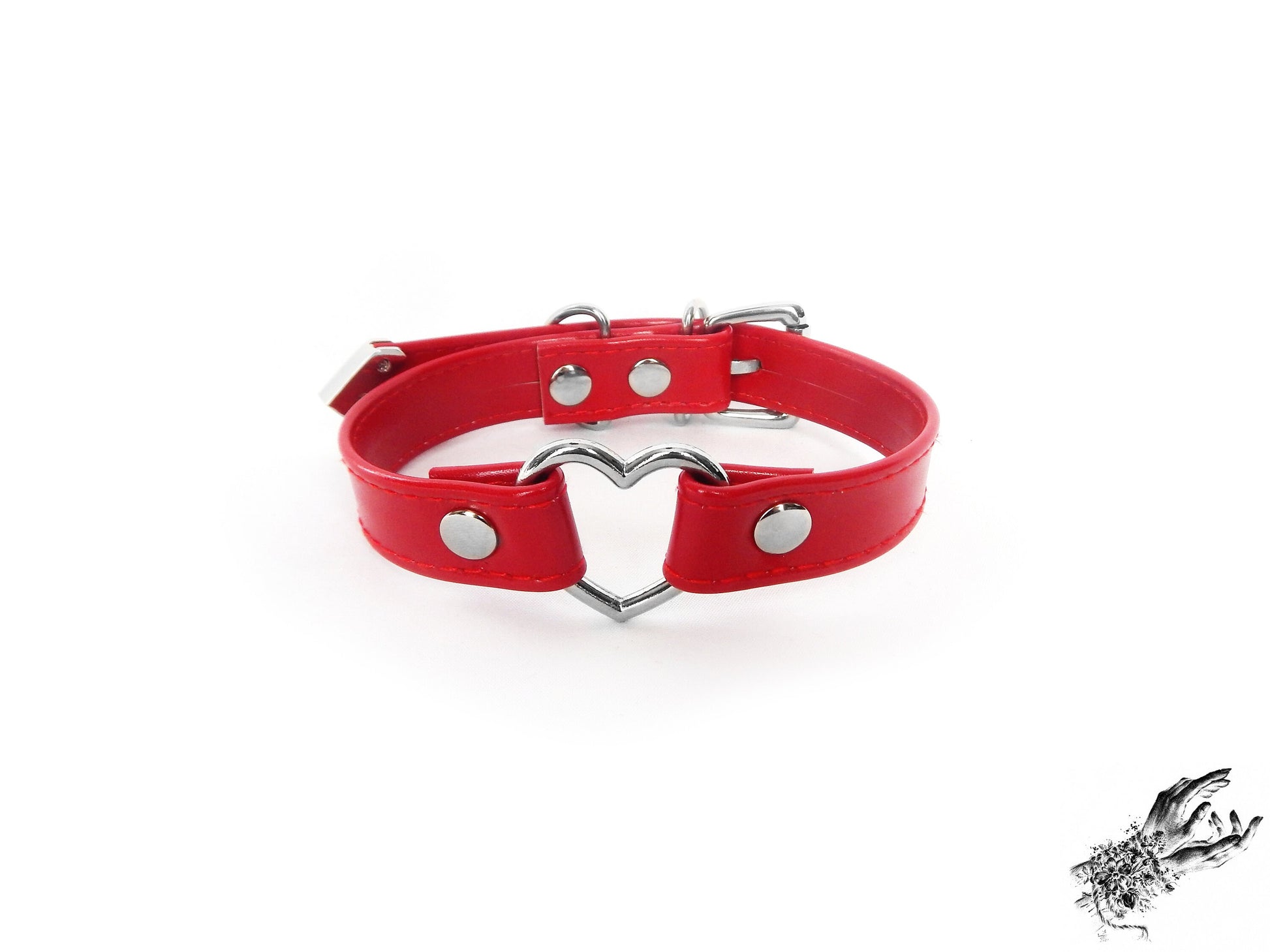Head-on photo of a red faux leather choker featuring a central silver tone heart ring and stainless steel plated hardware, with a buckle fastening and multiple sizing holes at the back. Displayed on a white background.