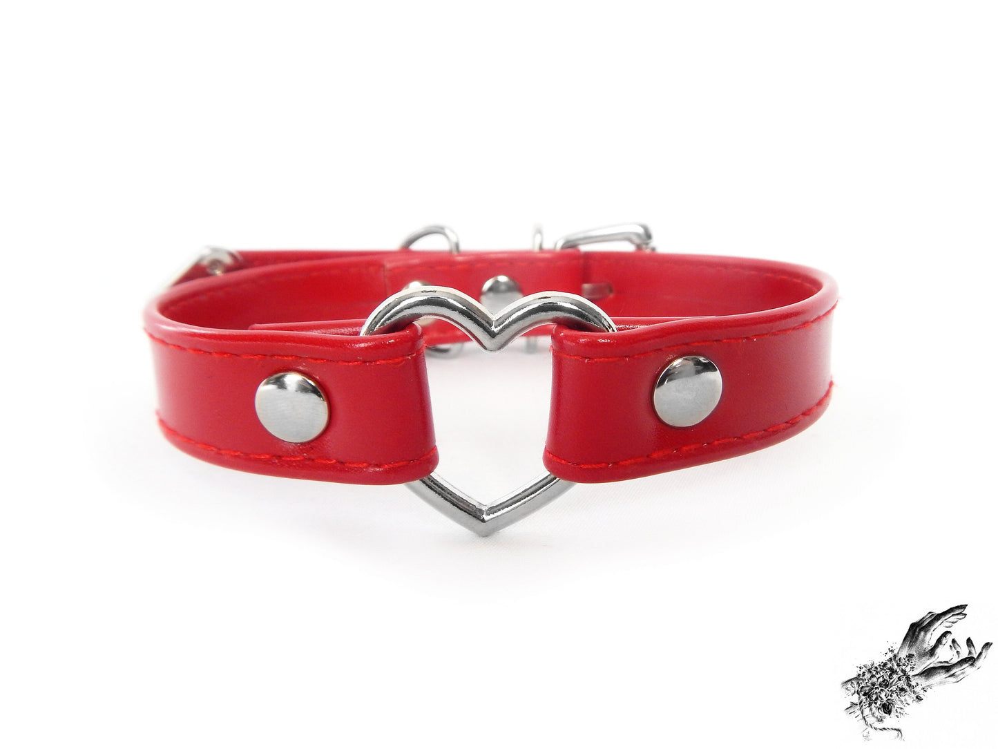 Close-up of a red faux leather choker featuring a central silver tone heart ring and stainless steel plated hardware, with a buckle fastening and multiple sizing holes at the back. Displayed on a white background.