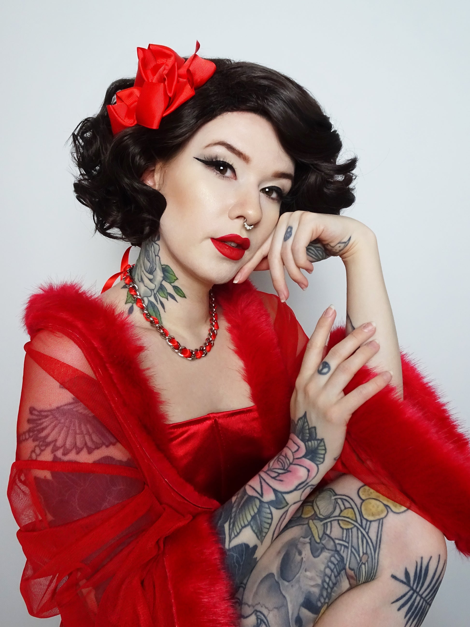Modelled photo of a silver stainless steel plated chain choker threaded with red satin ribbon. Styled with short brown curly hair and a red marabou nightgown in an alternative pin-up/rockabilly aesthetic.