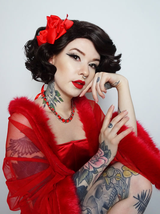 Modelled photo of a silver stainless steel plated chain choker threaded with red satin ribbon. Styled with short brown curly hair and a red marabou nightgown in an alternative pin-up/rockabilly aesthetic.