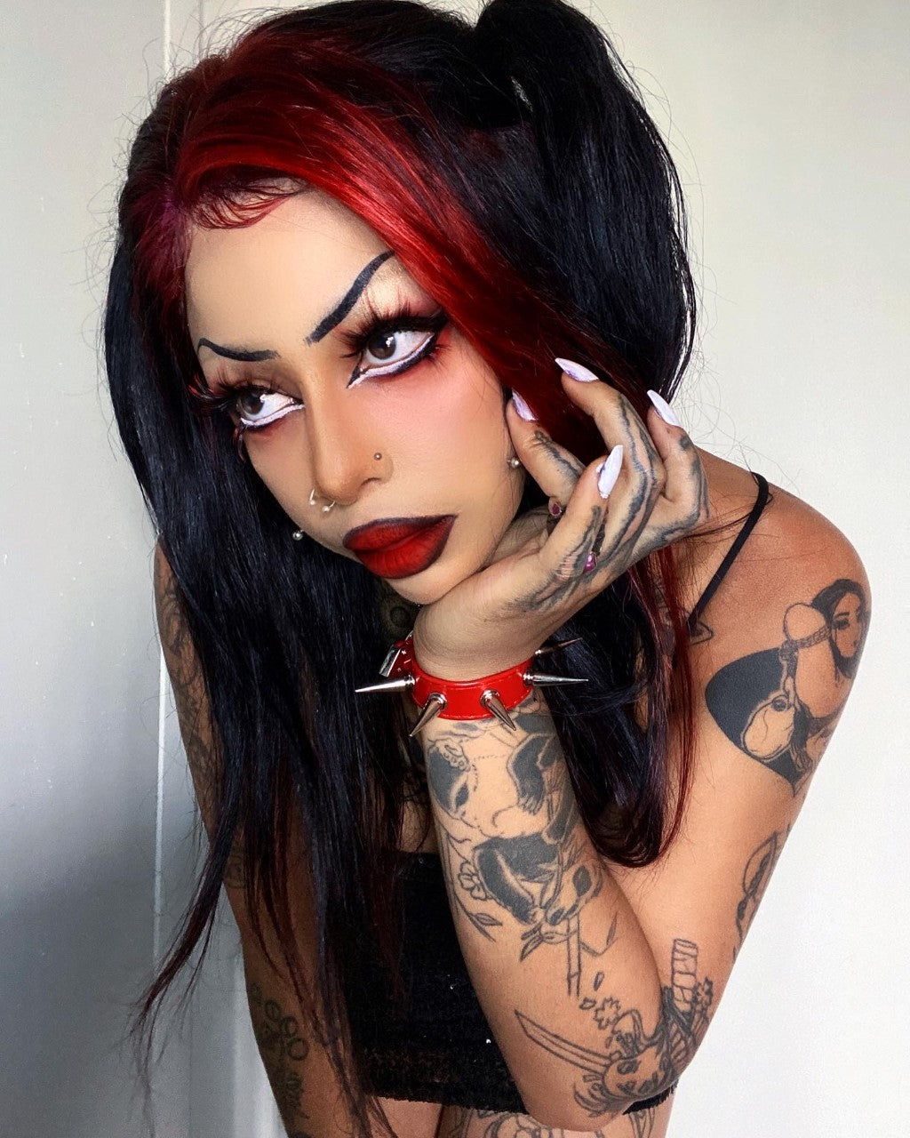 Modelled photo of red spike studded wristband, styled with bold gothic make-up, black and red hair and tattoos for a nu goth fashion look