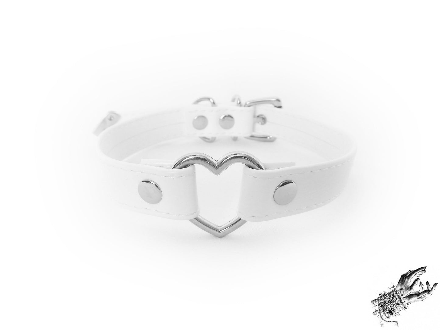Head-on photo of a white faux leather choker featuring a central silver heart ring and stainless steel plated hardware, with adjustable buckle and sizing holes at the back. Displayed on a white background.