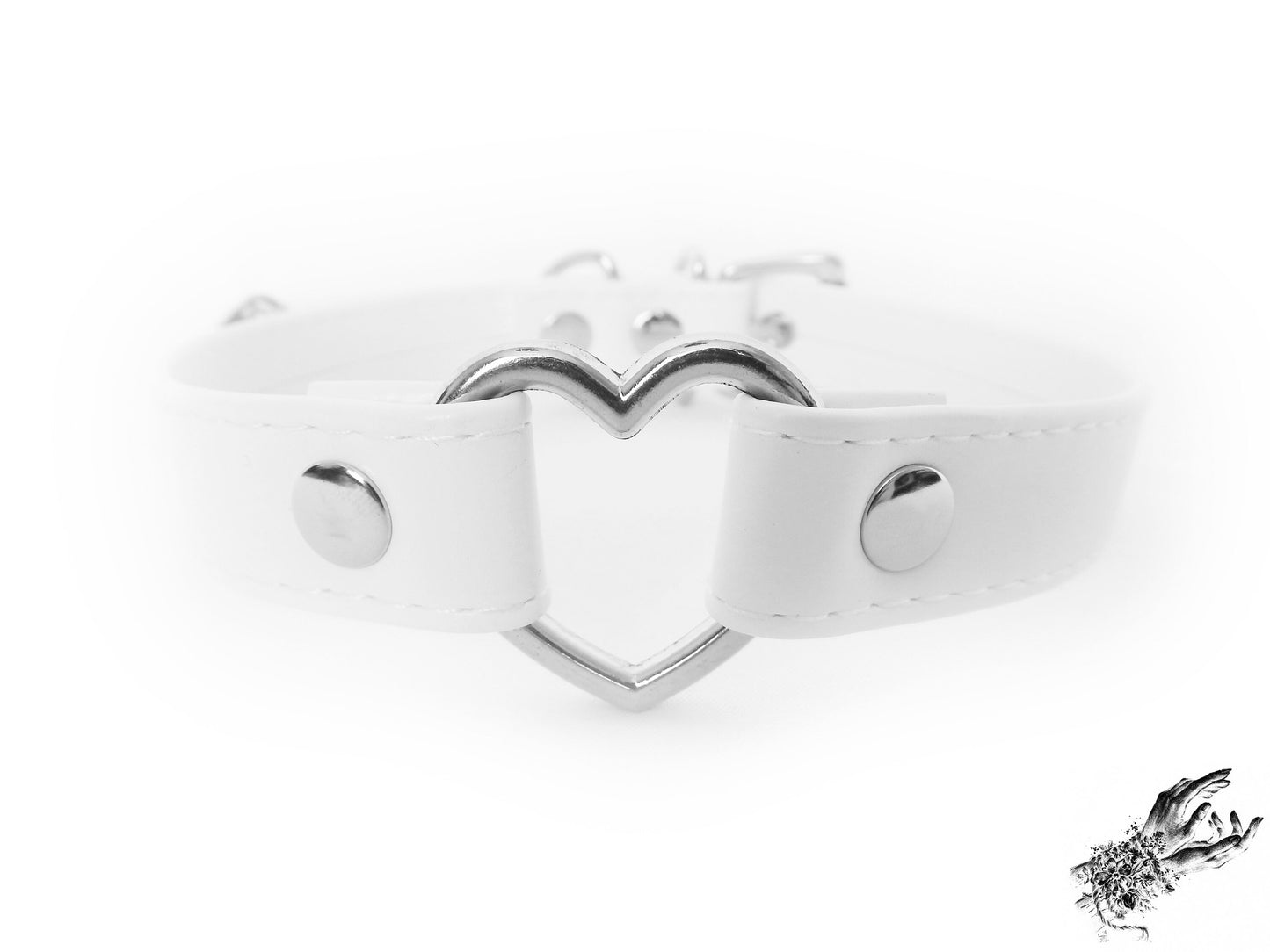 Close-up of a white faux leather choker featuring a central silver heart ring and stainless steel plated hardware, with adjustable buckle and sizing holes at the back. Displayed on a white background.