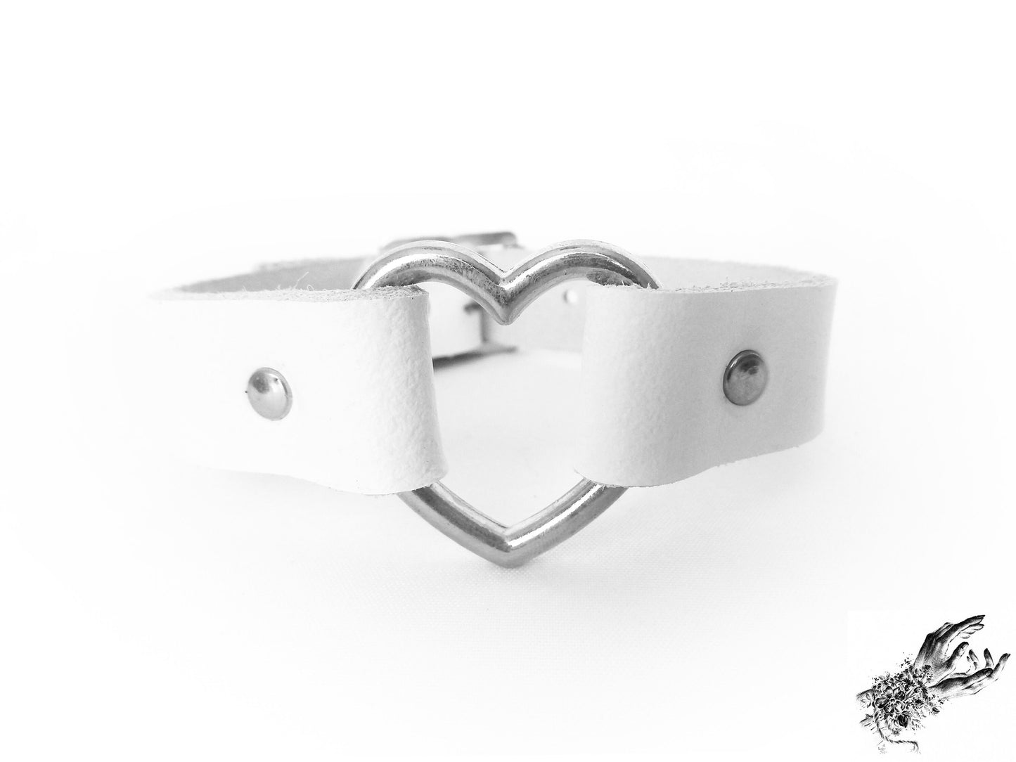 Close-up of the white leather wristband showing the silver heart ring and durable silver rivets