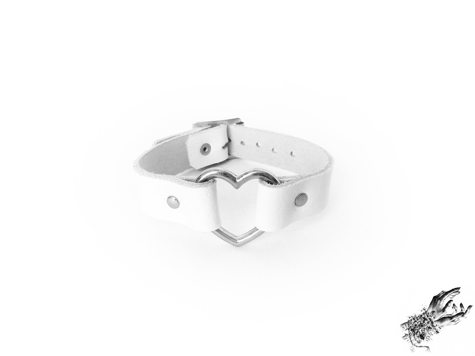White leather wristband with a central silver heart ring and adjustable buckle at the back