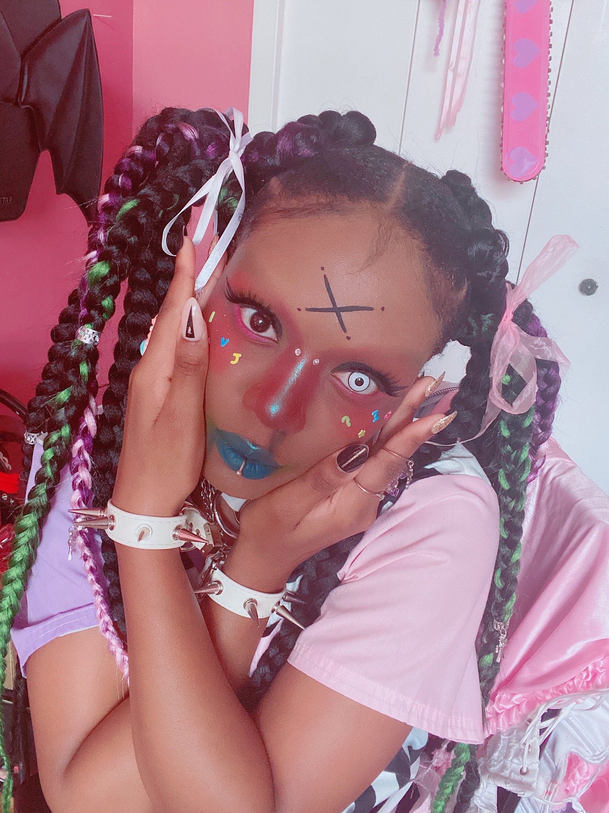 Modelled photo of a pair of white spike studded wristbands, styled with braided hair and bold make-up for a Harajuku fashion aesthetic